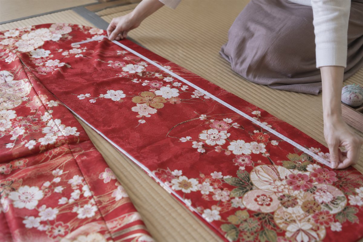 畳に広げた赤い振袖の寸法を、メジャーで測っている手元