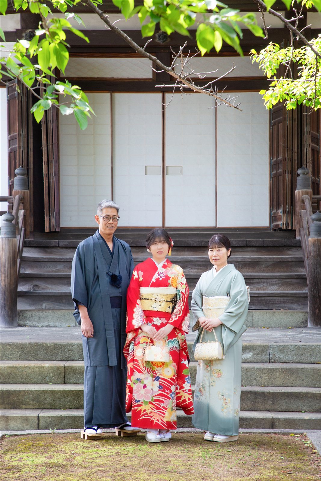 お寺の階段の前で、着物姿のご両親と振袖のお嬢様が並んで立つ家族写真