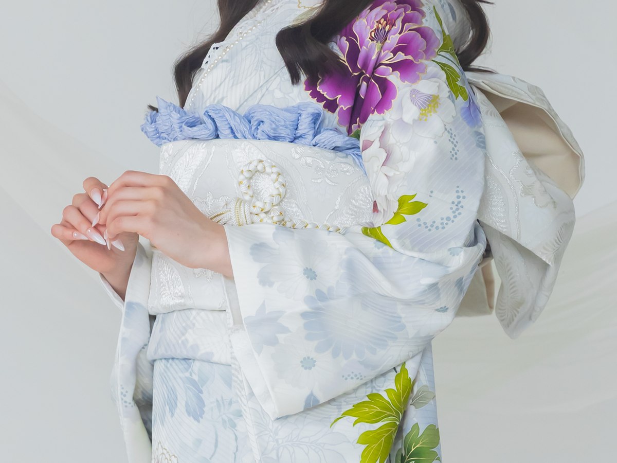 白地に紫の花の振袖の帯まわり。白の袋帯に、水色のフリルの帯揚げと白の帯締めを合わせている