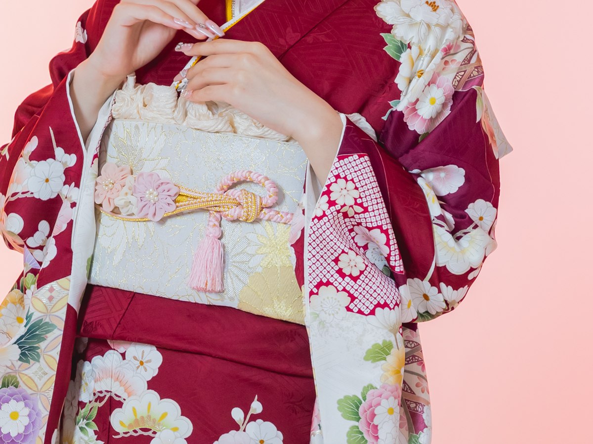 赤の古典柄の振袖の帯まわり。白銀の袋帯に、ピンクの帯締めと花の帯飾りを合わせている