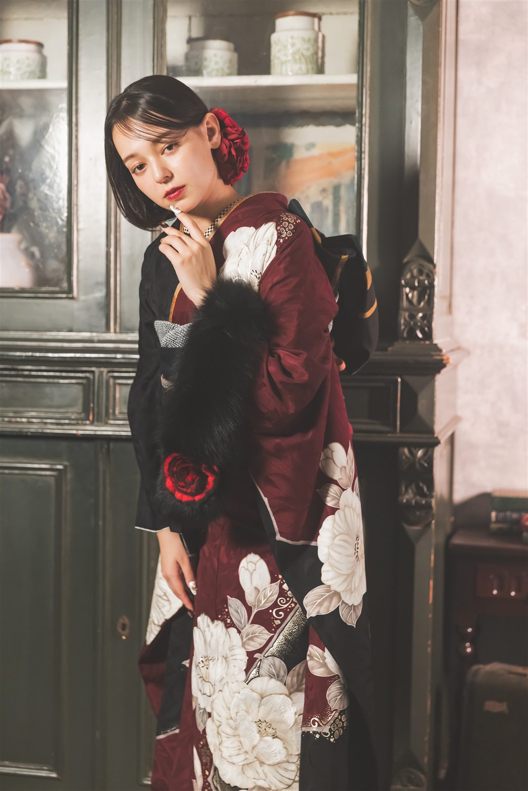 黒髪のボブ風スタイルに深紅の花の髪飾りをつけ、黒のファーのショールを合わせた大正ロマン振袖